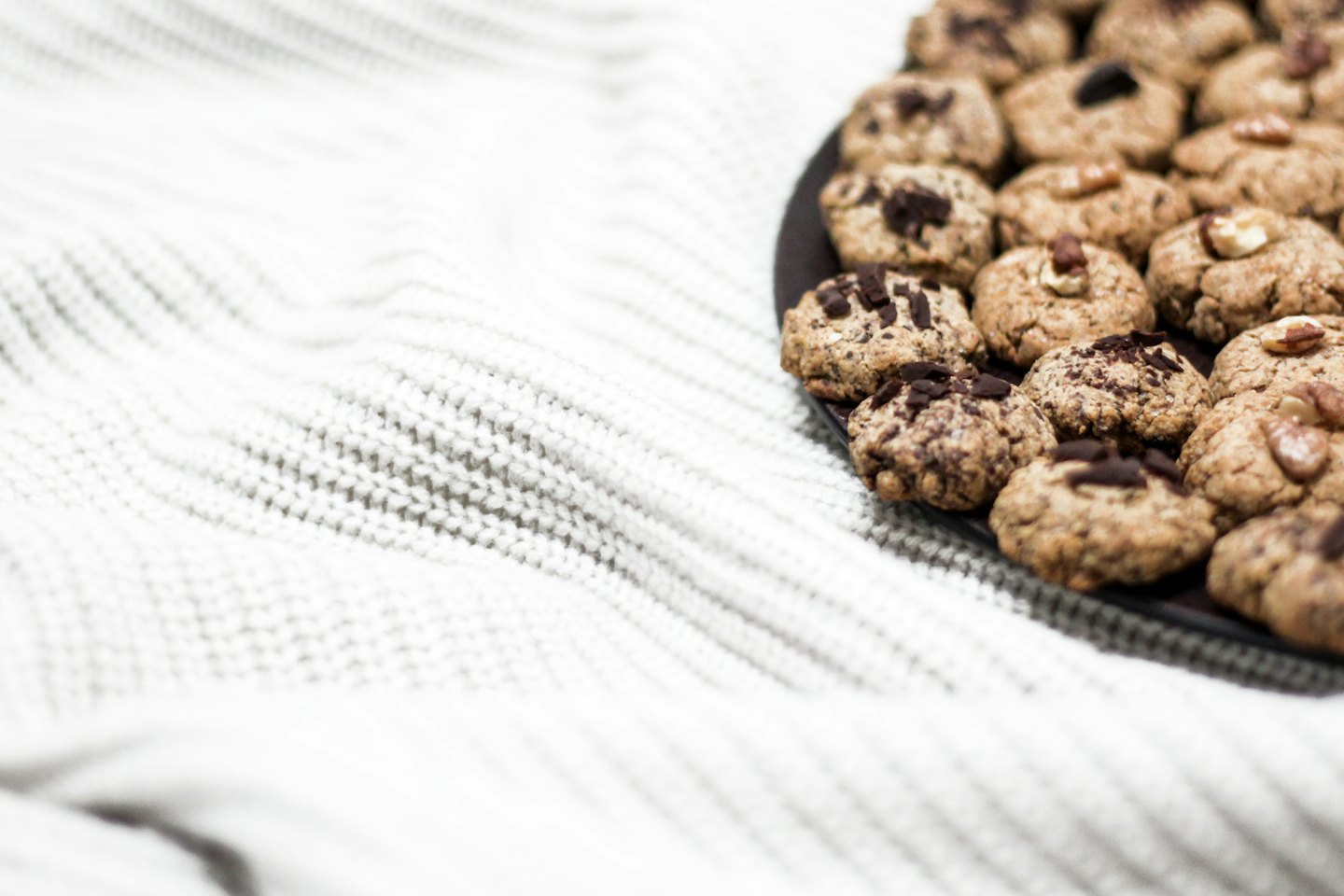 Homemade cookies sit on a plate atop a white blanket.