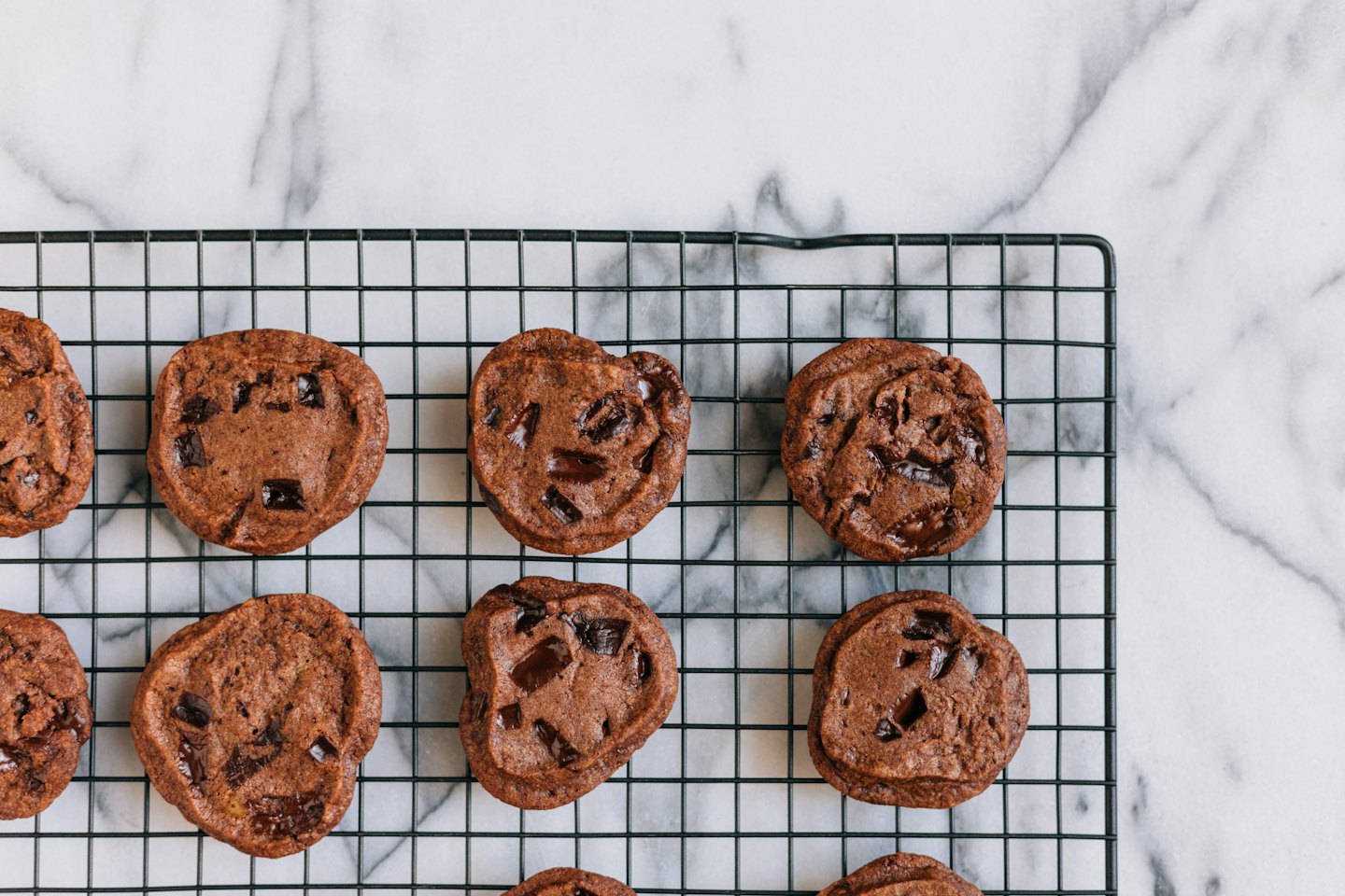 Freshly baked chocolate chip cookies on a black wire cooling rack.