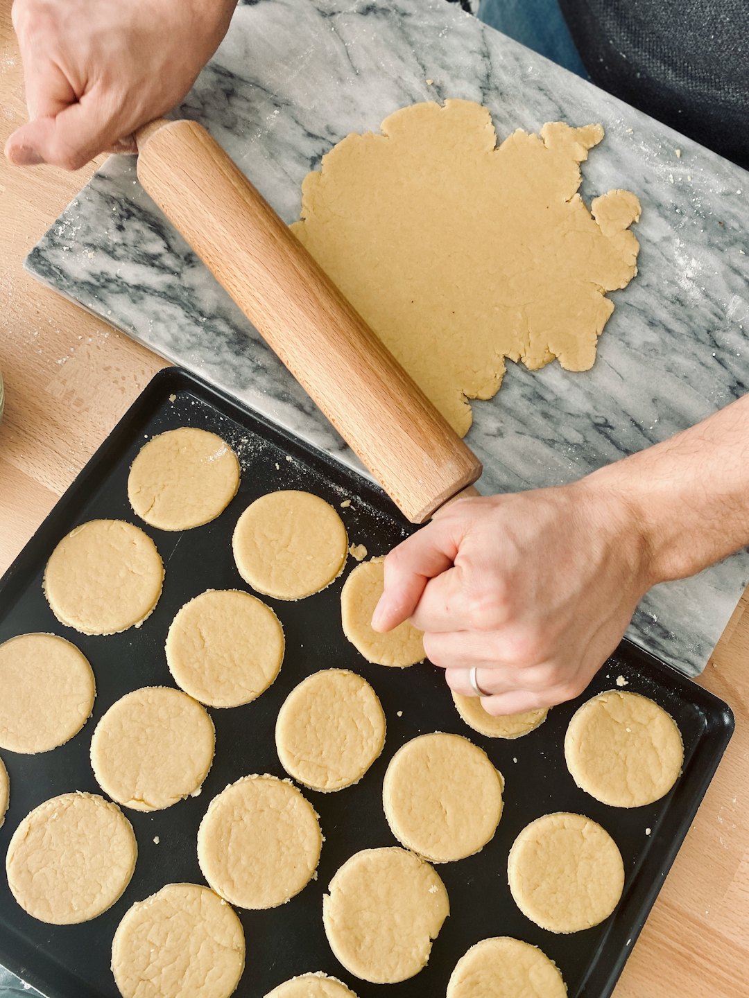 Hands rolling out dough and placing circular cookies on a tray.