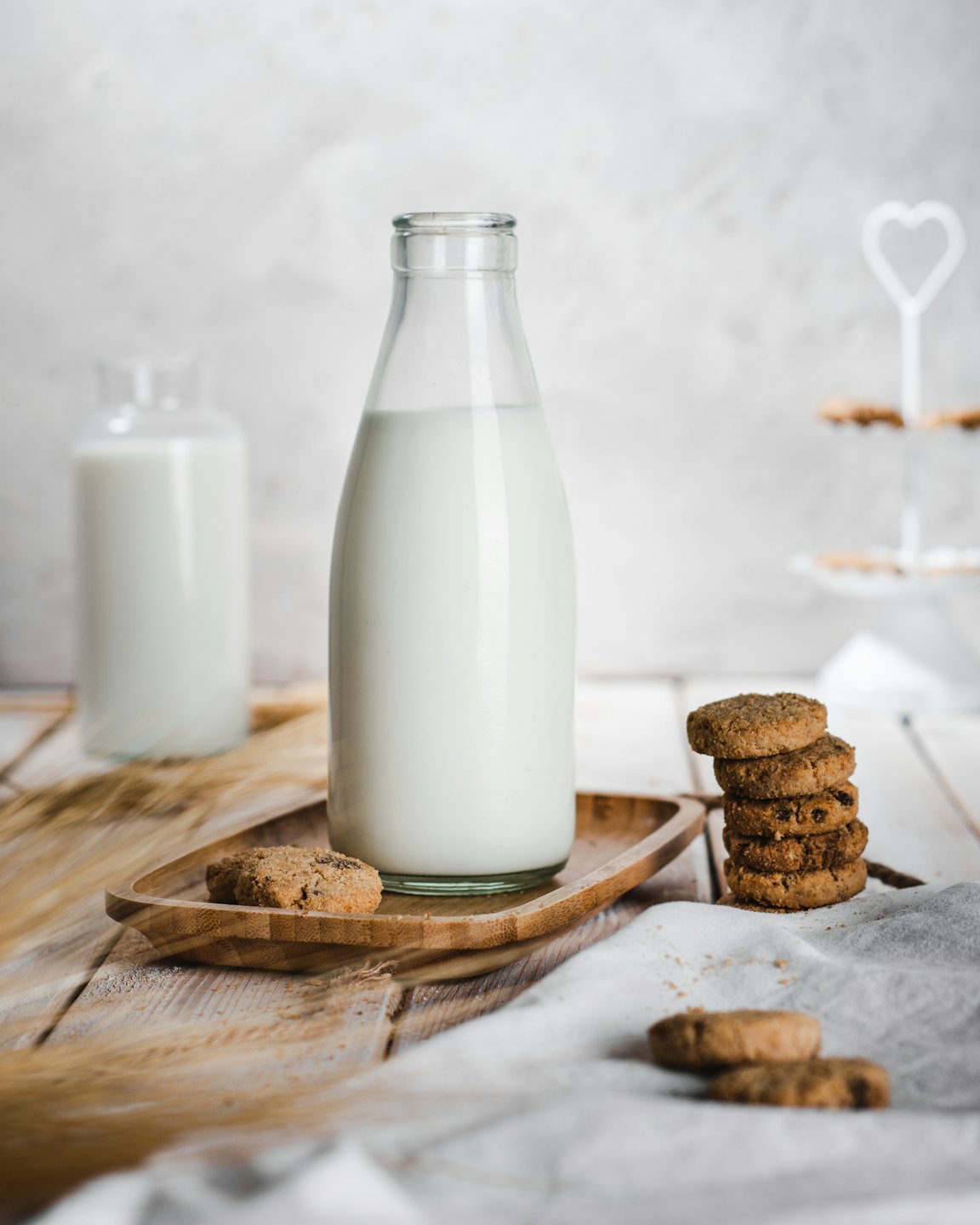 Two bottles of milk with cookies on a wooden tray.